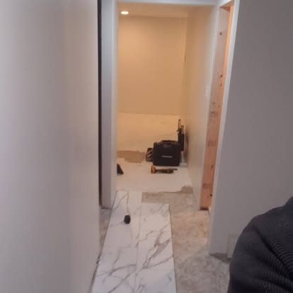 Narrow hallway with marble flooring leading to bright room with recessed lighting and black armchair