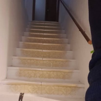 Indoor staircase with light stone steps leading upward, white walls, and wooden handrail on right side