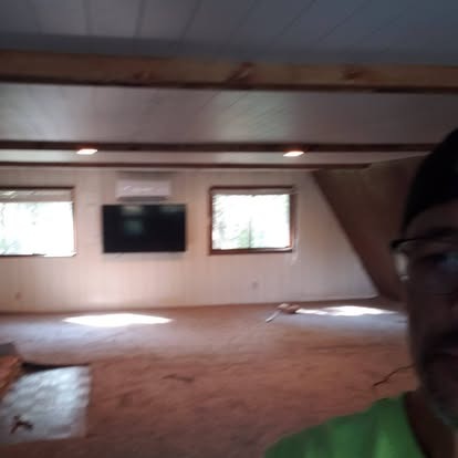 Spacious unfinished attic room with exposed beams, windows, and wooden flooring