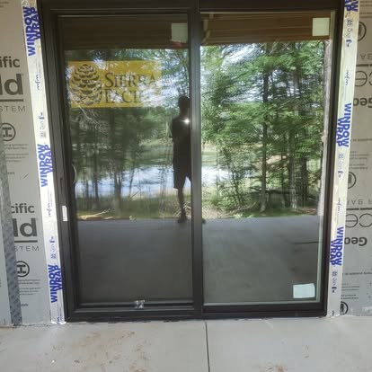 Double glass sliding doors with dark frame overlooking wooded lake view during installation