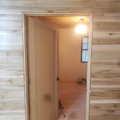 Interior doorway with frosted glass door opening into a room with wood paneling and ceiling light