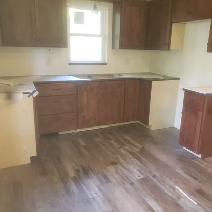 Empty kitchen with brown cabinets, beige walls, and wood-look flooring with window