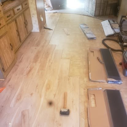Hardwood flooring installation in progress with planks, underlayment, and tools on kitchen subfloor