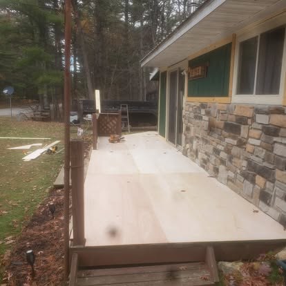 Concrete patio extending from stone and green siding home with wooded yard