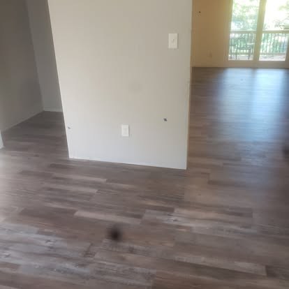 Empty apartment interior with wood flooring, white walls, and glass doors leading to balcony