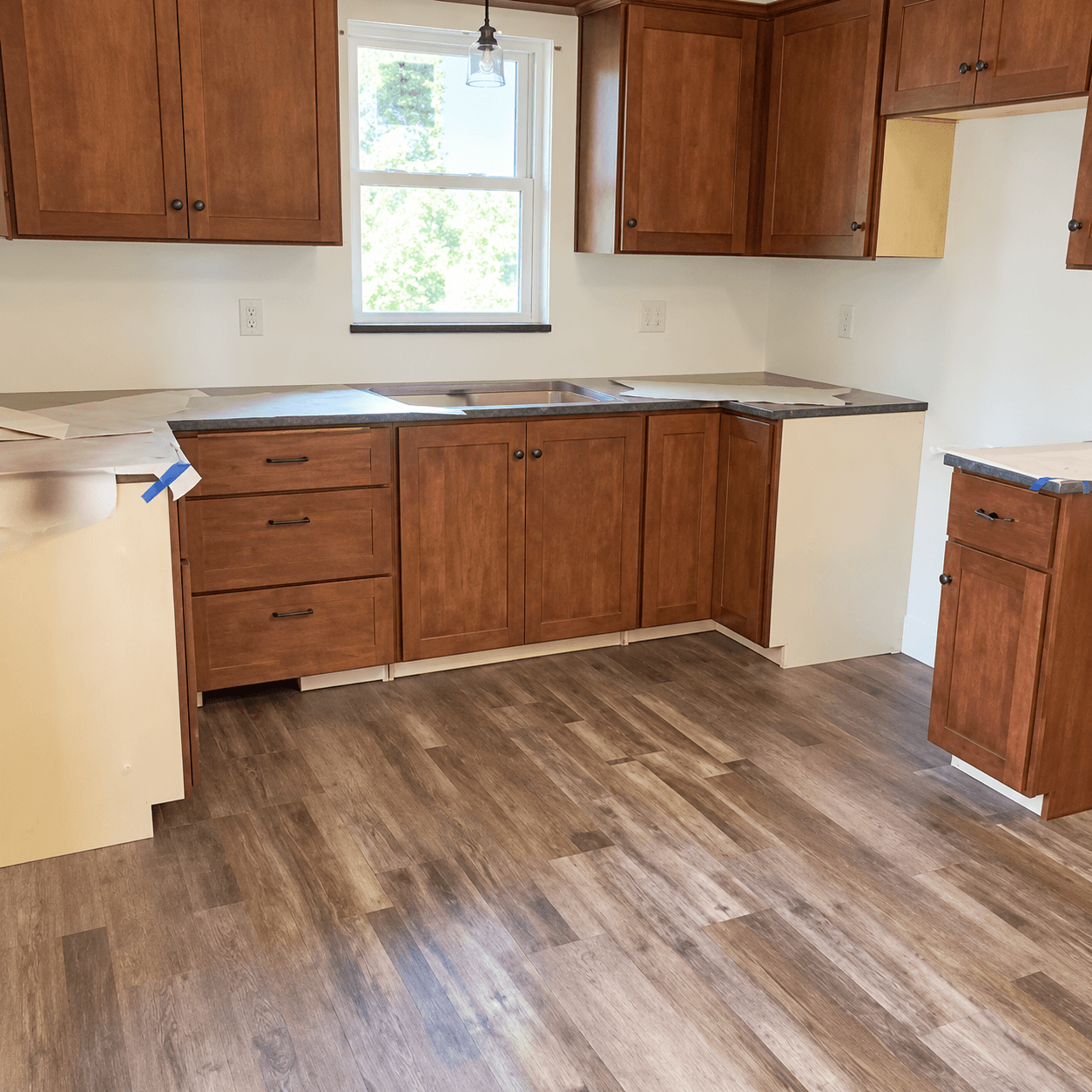 Kitchen with wooden cabinets, dark countertops, wood flooring, and window
