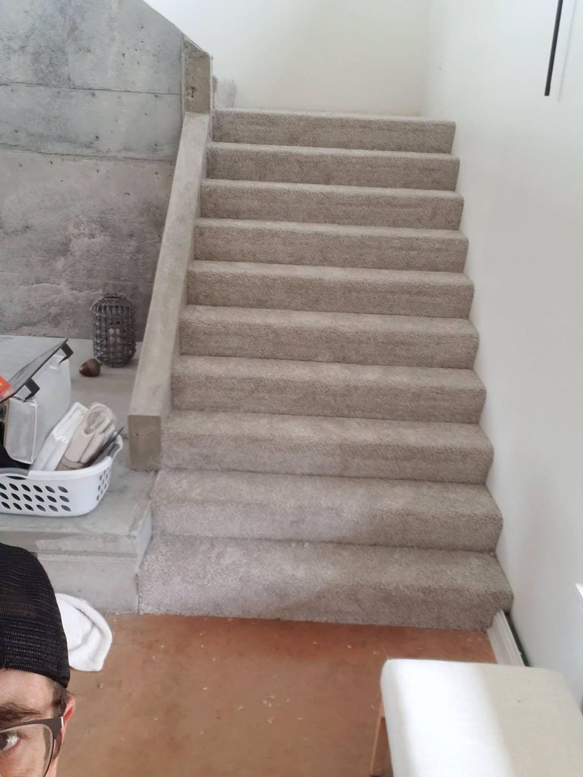 Carpeted staircase with beige steps, white walls, and concrete wall on left side
