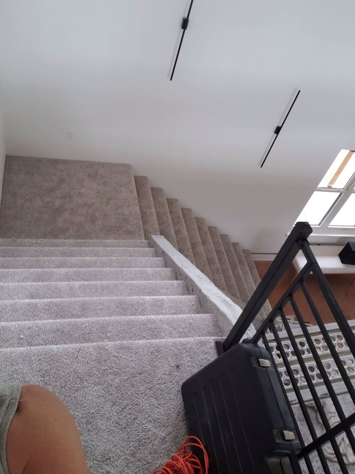 Modern staircase with gray carpet and white trim leading upward in attic space with skylight