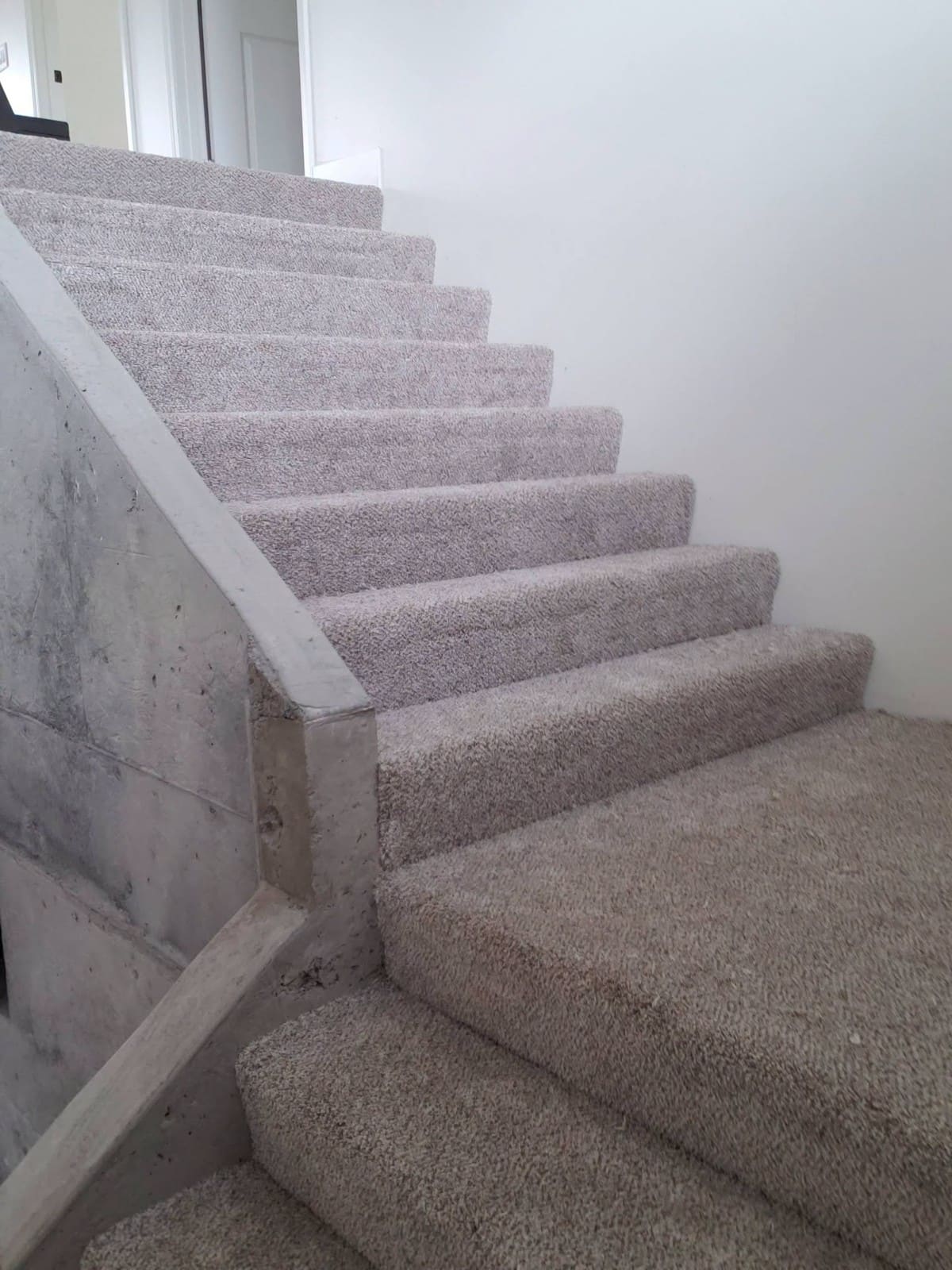 Newly installed gray carpet on residential staircase with white trim and concrete wall
