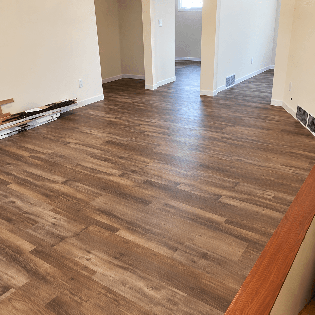 Spacious interior room with laminate wood flooring, white walls, and multiple doorways leading to adjacent rooms